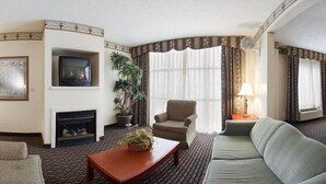 Une chambre d’hôtel équipée d’un canapé, d’un fauteuil, d’une télévision, d’une cheminée et de grandes fenêtres avec des rideaux.