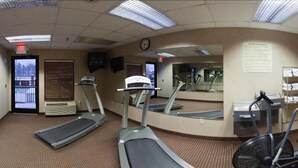 Et fitnesscenter med løbebånd, et spejl og en ventilator.