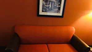 Et rum med en orange sofa, en billedramme over sofaen og en lampe til højre.