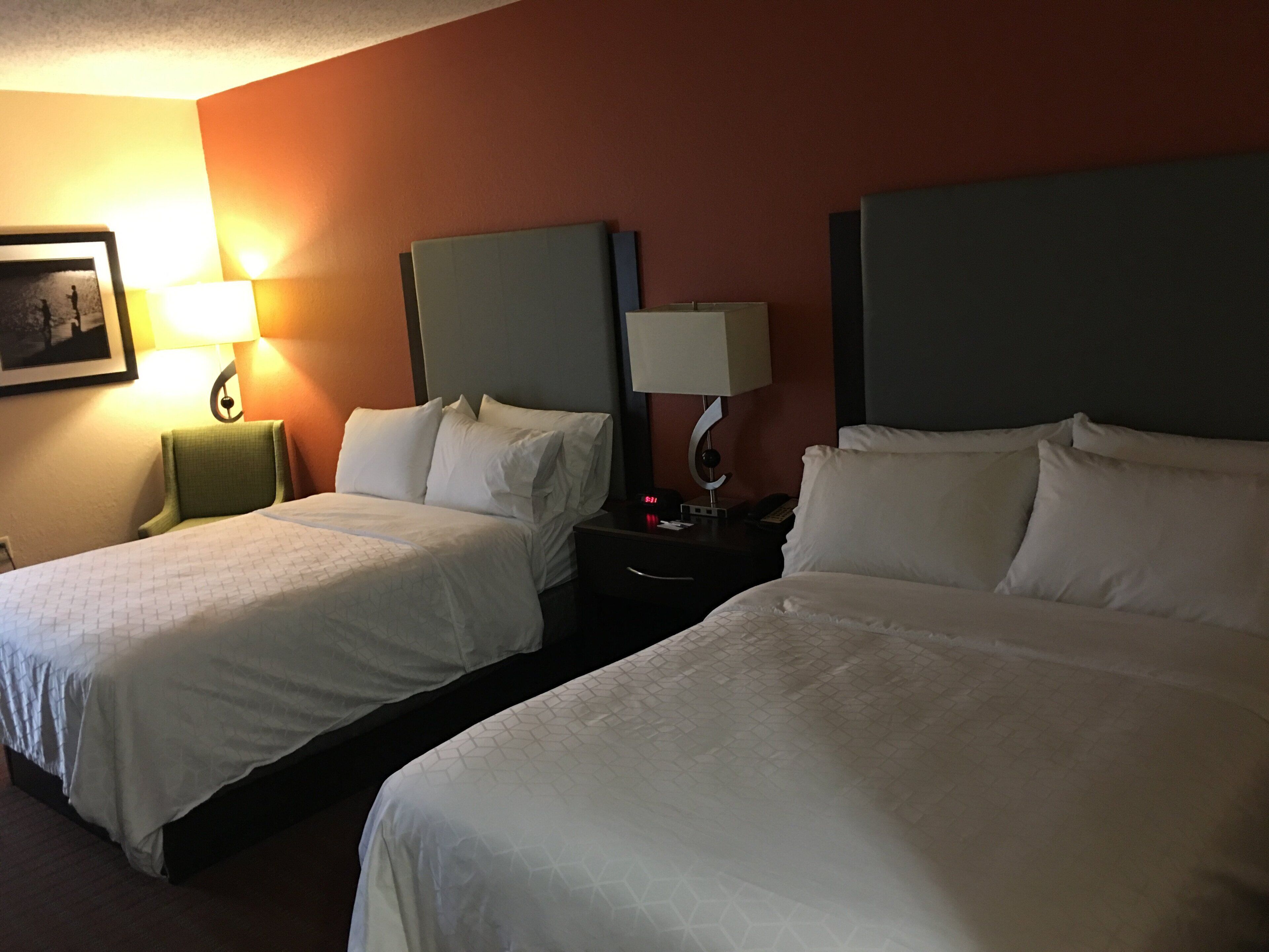 A hotel room with two beds, a nightstand with a lamp, and a framed picture on the wall.