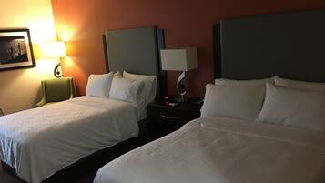 A hotel room with two beds, a nightstand with a lamp, and a framed picture on the wall.