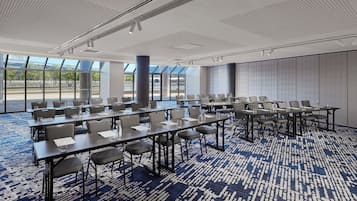 Un salón de conferencias con varias mesas y sillas, ventanas amplias y una alfombra estampada.