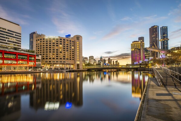 A waterfront cityscape with modern buildings, including a hotel with a prominent sign.