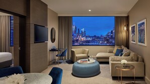 A modern hotel room with a large window offering a city view, a flat-screen TV, a sofa, a coffee table, and a small side table. - Crowne Plaza Melbourne by IHG (Docklands)