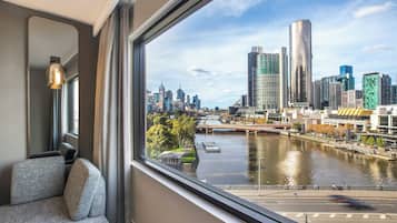 A modern hotel room with a large window offering a view of a city skyline and a river.