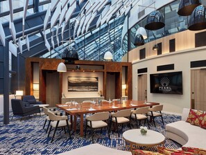 A modern hotel lobby with a large conference table, seating, and a TV screen displaying the hotel name. - Crowne Plaza Melbourne by IHG (Docklands)