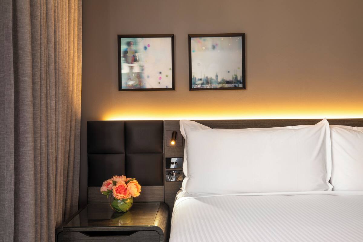 A hotel room with a bed, a nightstand with a vase of flowers, and two abstract paintings on the wall.