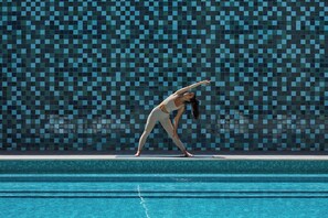 A person performing a yoga pose on a poolside with a tiled wall in the background. - Crowne Plaza Melbourne by IHG (Docklands)