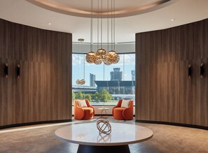 A modern interior with a round table, two orange chairs, and a city view through large windows. - Crowne Plaza Melbourne by IHG (Docklands)