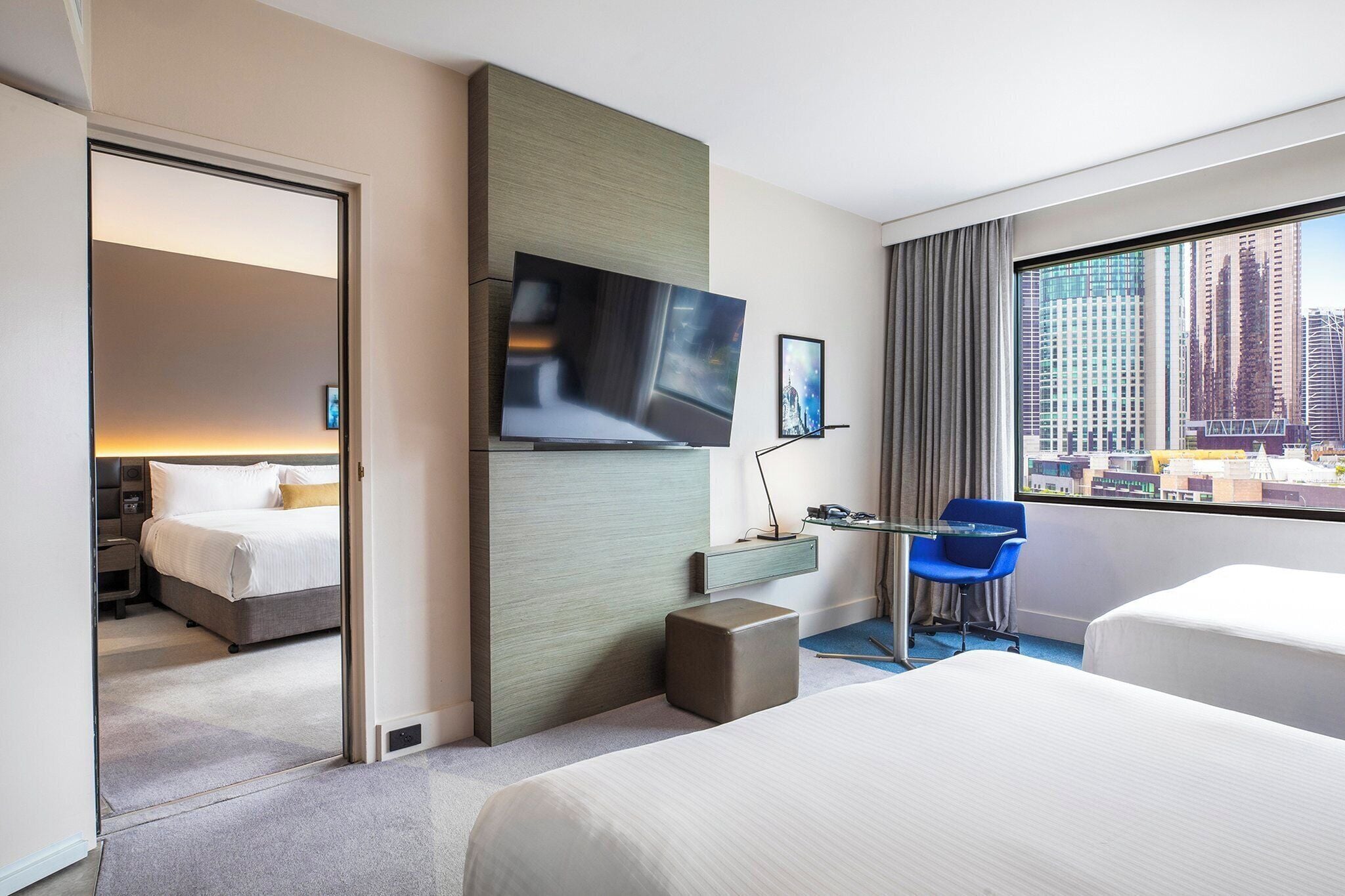A hotel room with a bed, a desk, a chair, a TV, and a large window with a city view.