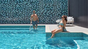 A swimming pool with tiled walls and a lounge area with a white chair and a patterned cushion. - Crowne Plaza Melbourne by IHG (Docklands)