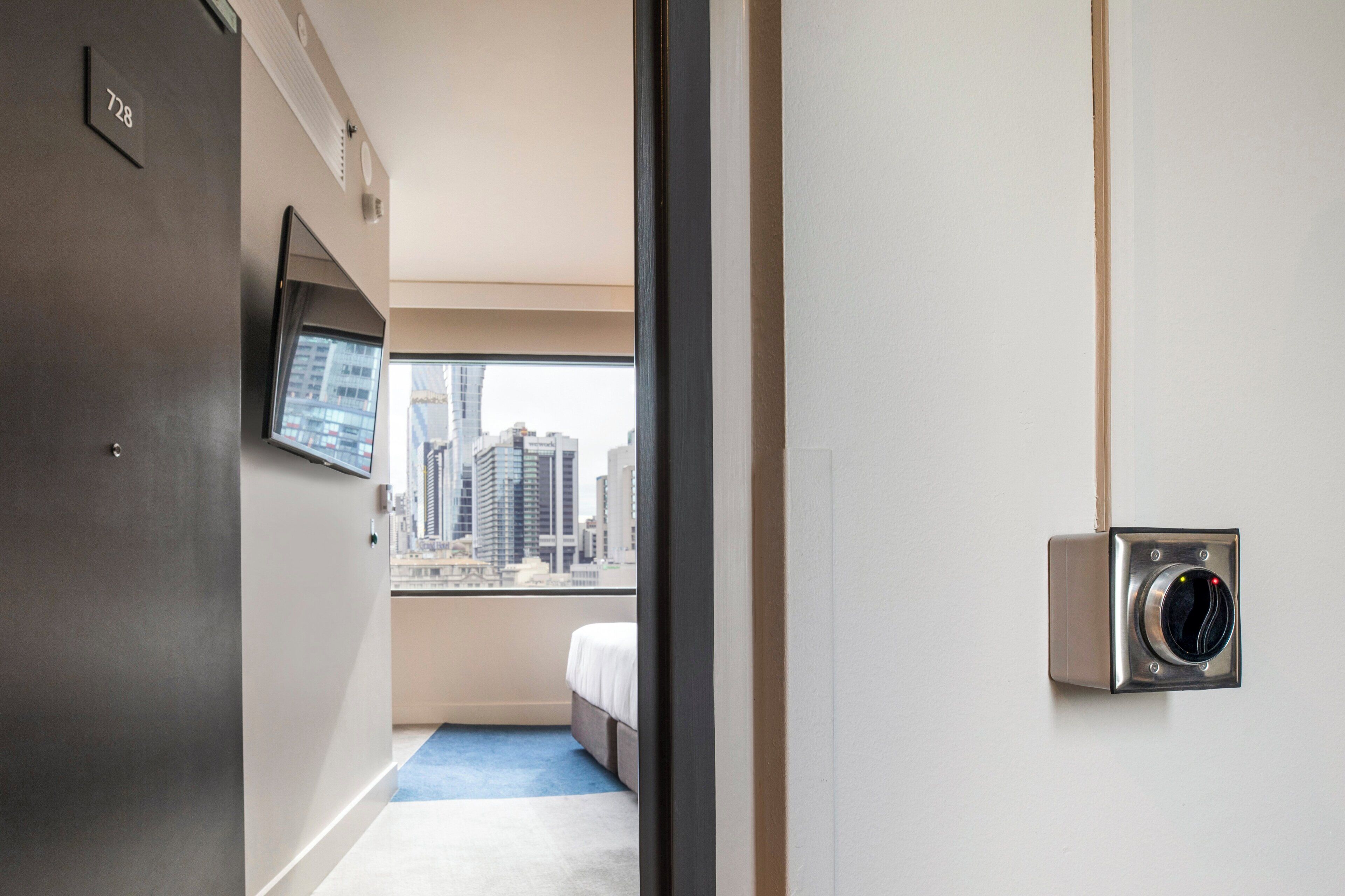 A hotel room with a bed, a TV mounted on the wall, and a window with a city view.