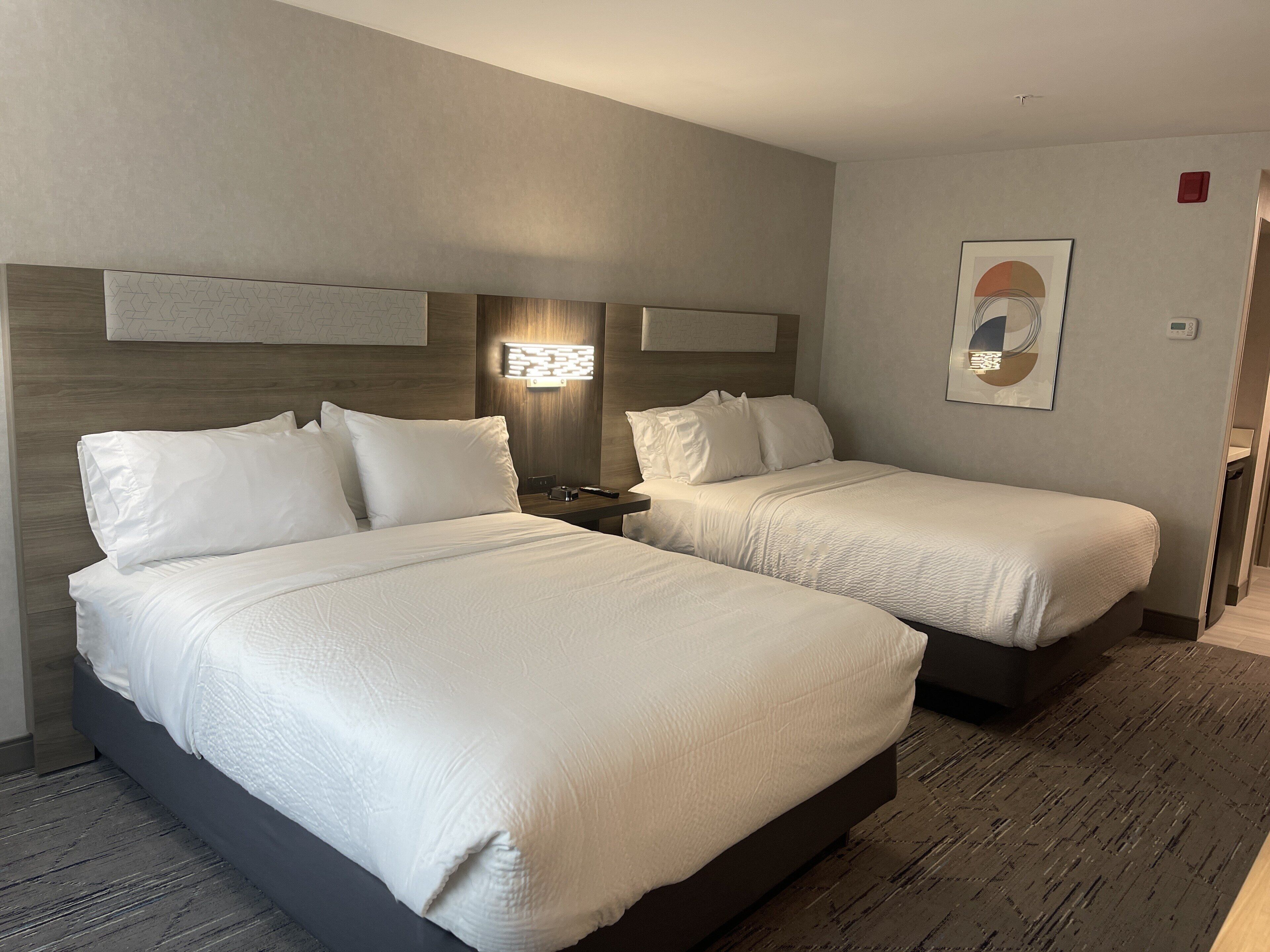Ein Hotelzimmer mit zwei Betten, einem Nachttisch, einer Wandleuchte und einem gerahmten Bild.
