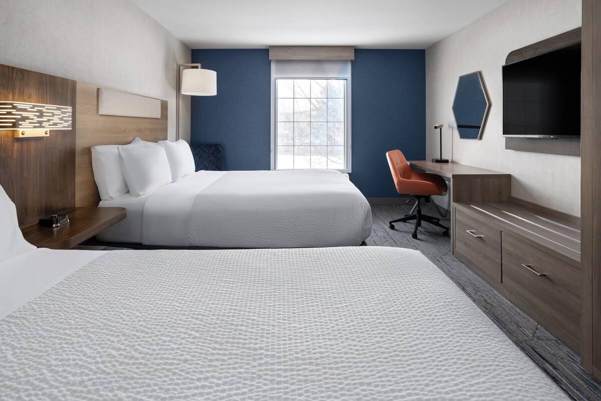 A hotel room with two beds, a desk, a TV, and a window.