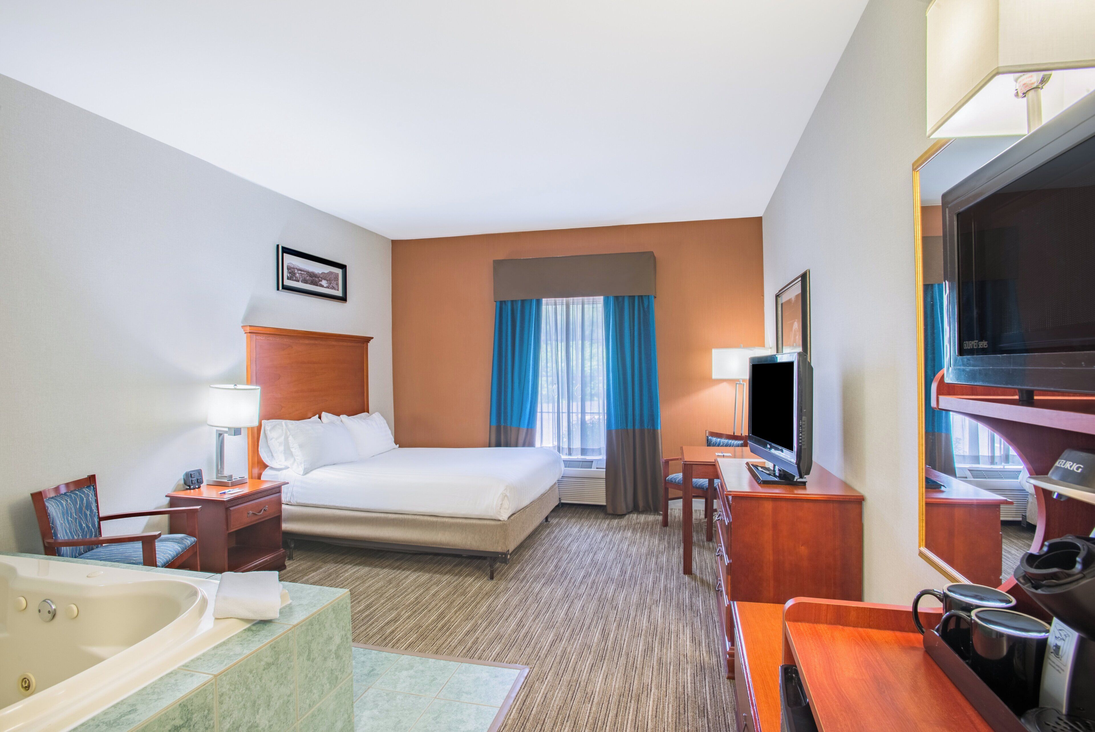 A hotel room with a bed, a desk, a television, a bathroom with a bathtub, and a large window with curtains.
