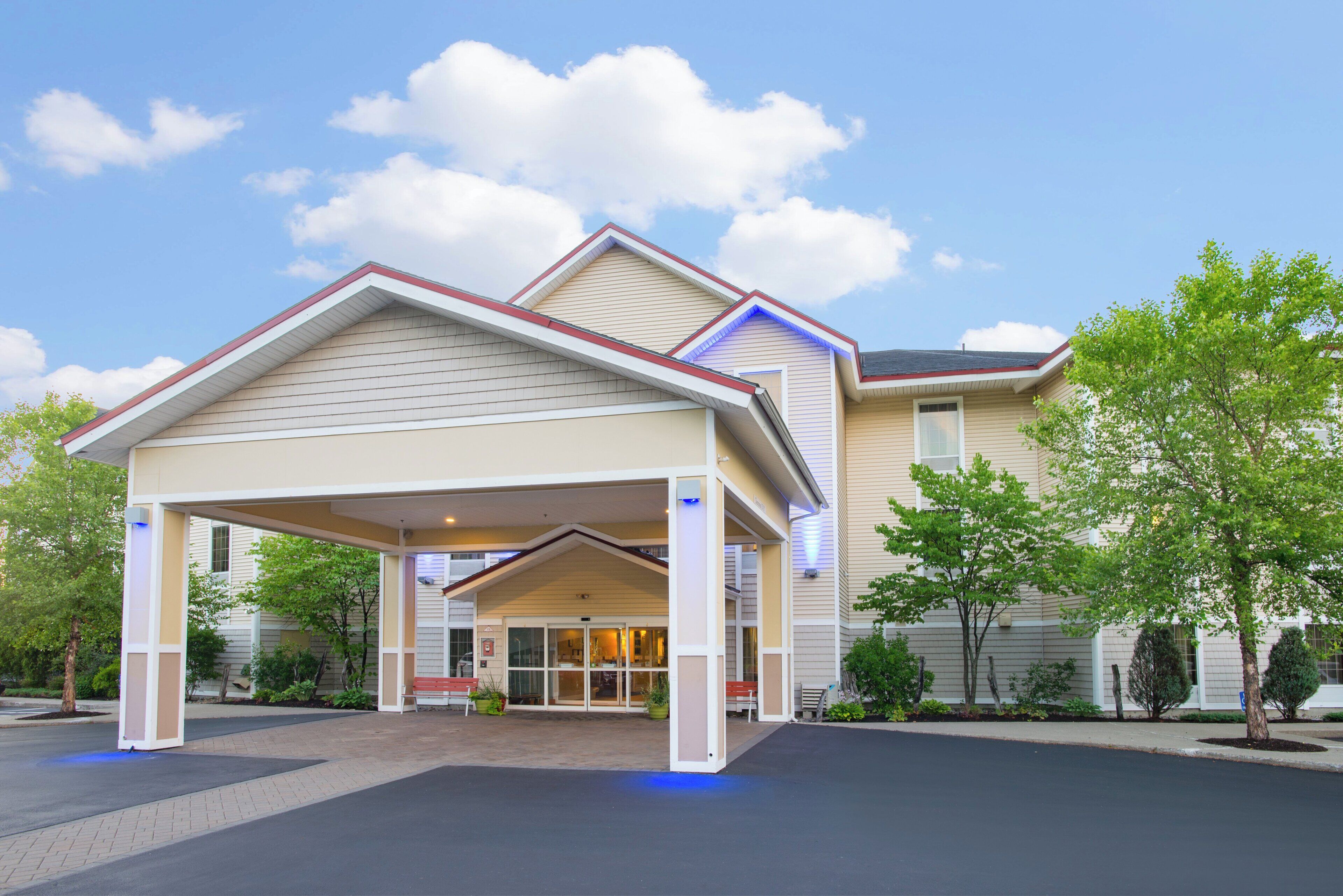 A hotel with a covered entrance, a parking lot, and a landscaped area with trees.