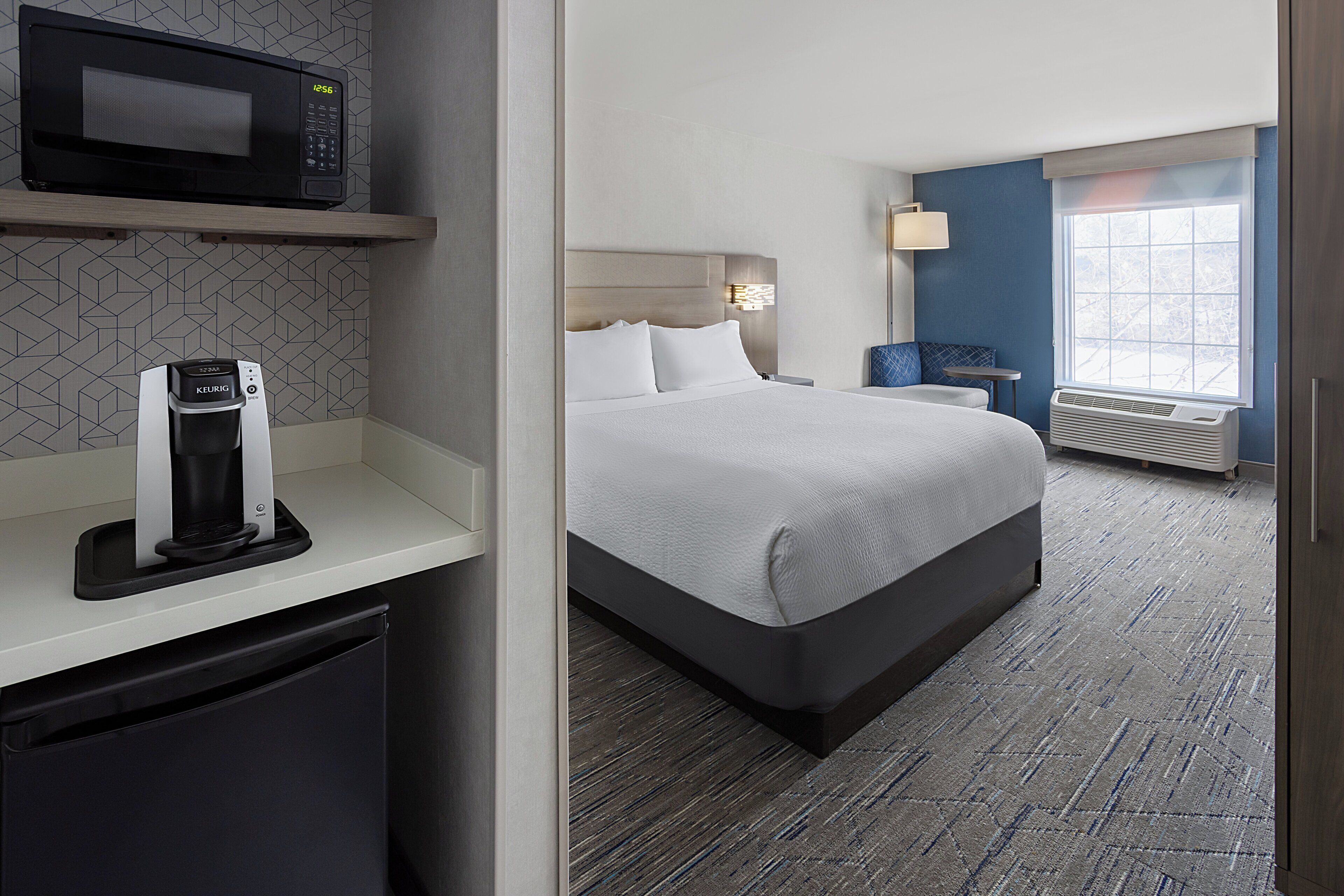 A hotel room with a bed, a microwave, a coffee maker, a nightstand, and a window with a view.