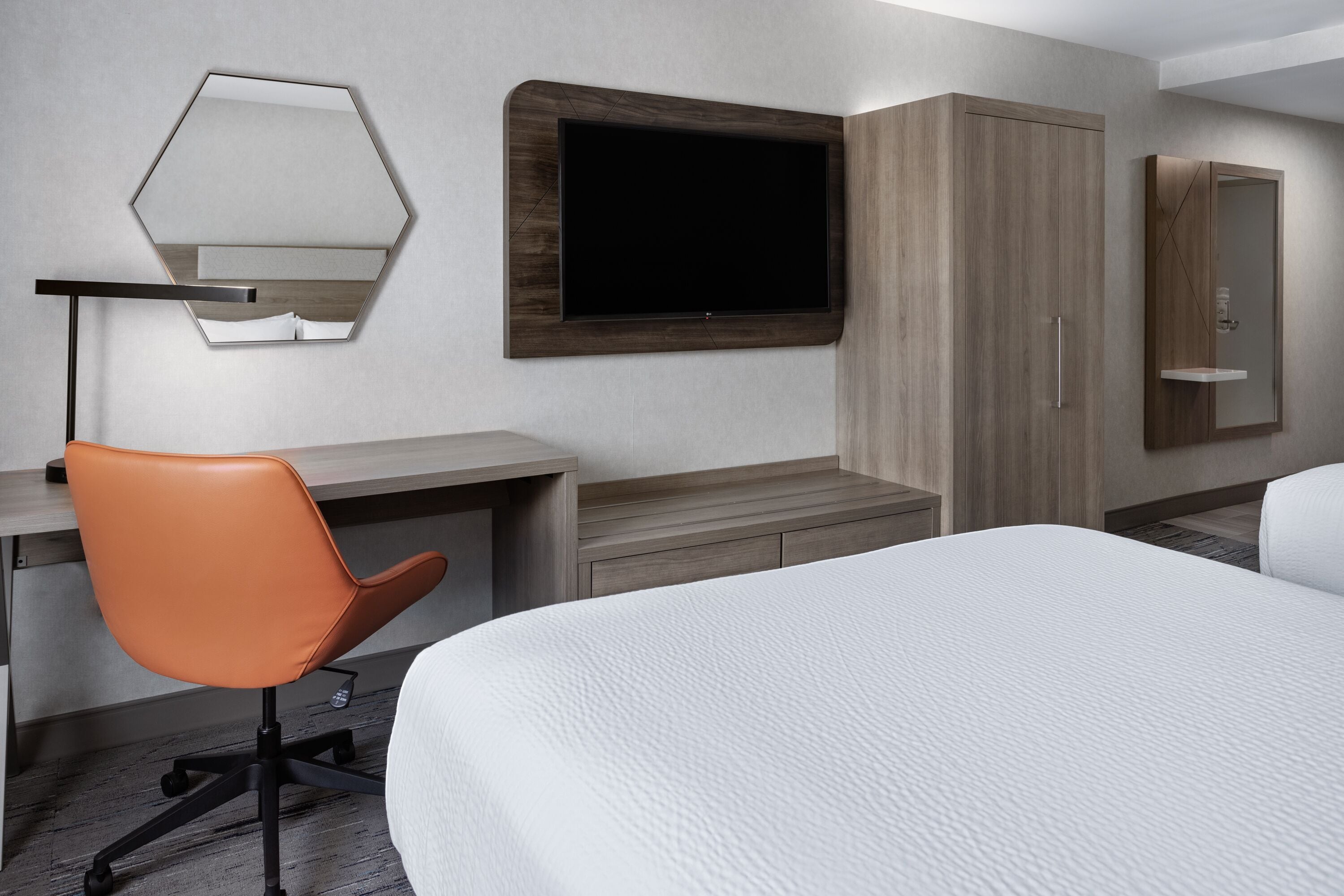 Una habitación de hotel con cama, escritorio, sillón naranja, televisor y armario.