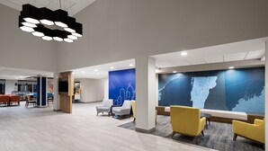 Um hall amplo com móveis modernos, um grande painel digital de mapa e um teto alto com iluminação geométrica.