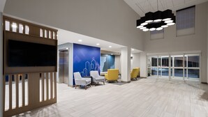 Um lobby espaçoso com uma grande TV de tela plana, assentos modernos e uma ampla janela com vista para a cidade.