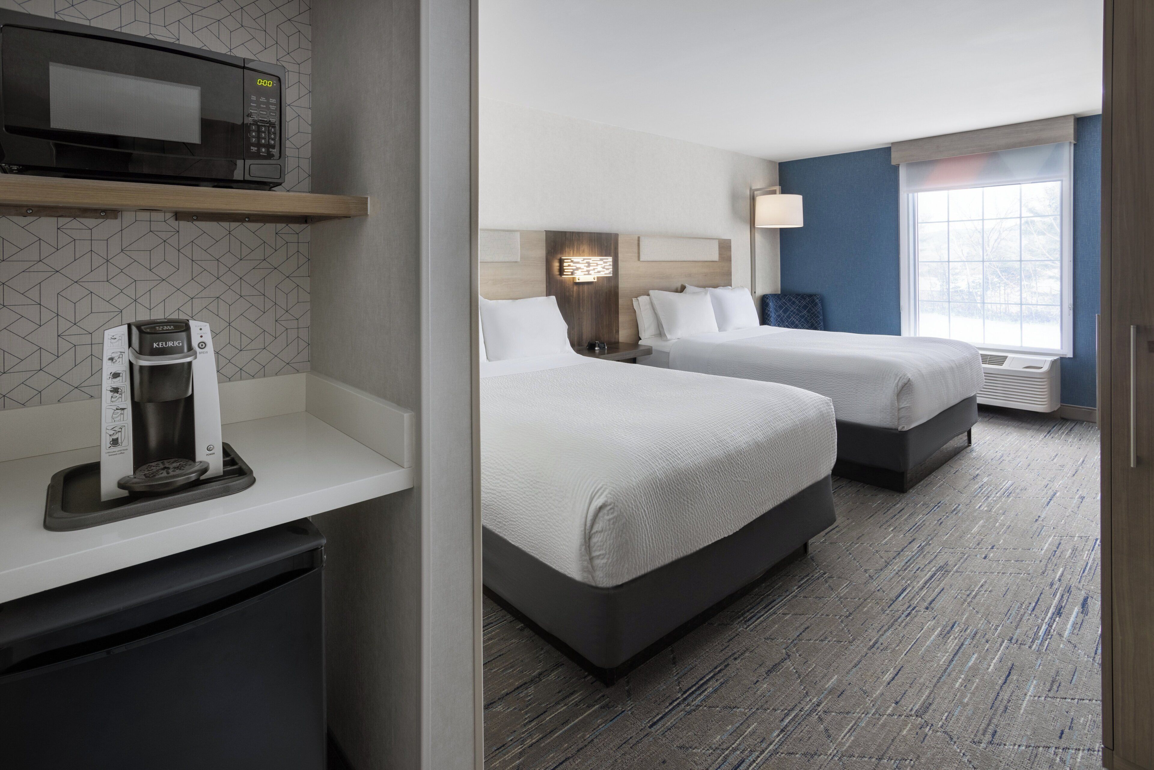 A hotel room with two beds, a microwave, a coffee maker, and a window with a view.
