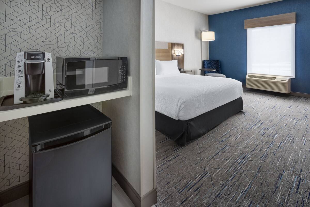 A hotel room with a bed, a microwave, a coffee maker, and a small trash bin.