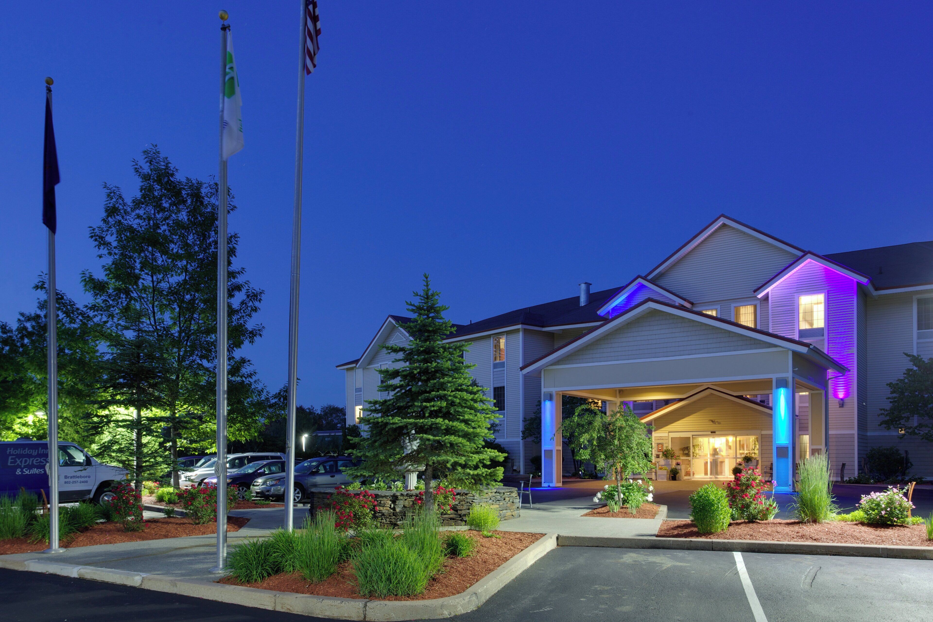 A hotel entrance with a covered walkway, flag poles, and a parking lot.