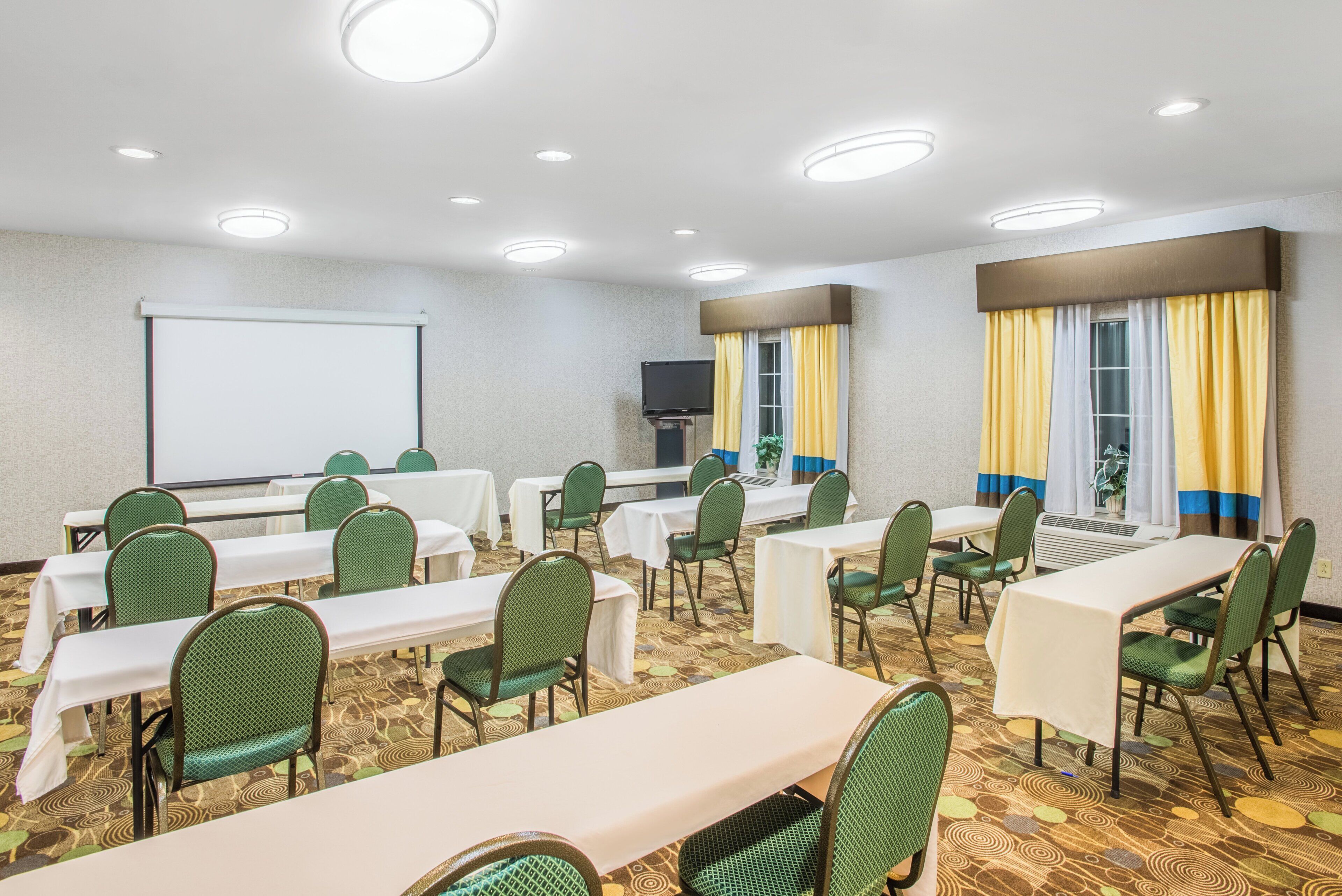 A conference room with tables and chairs, a projector screen, and a television.