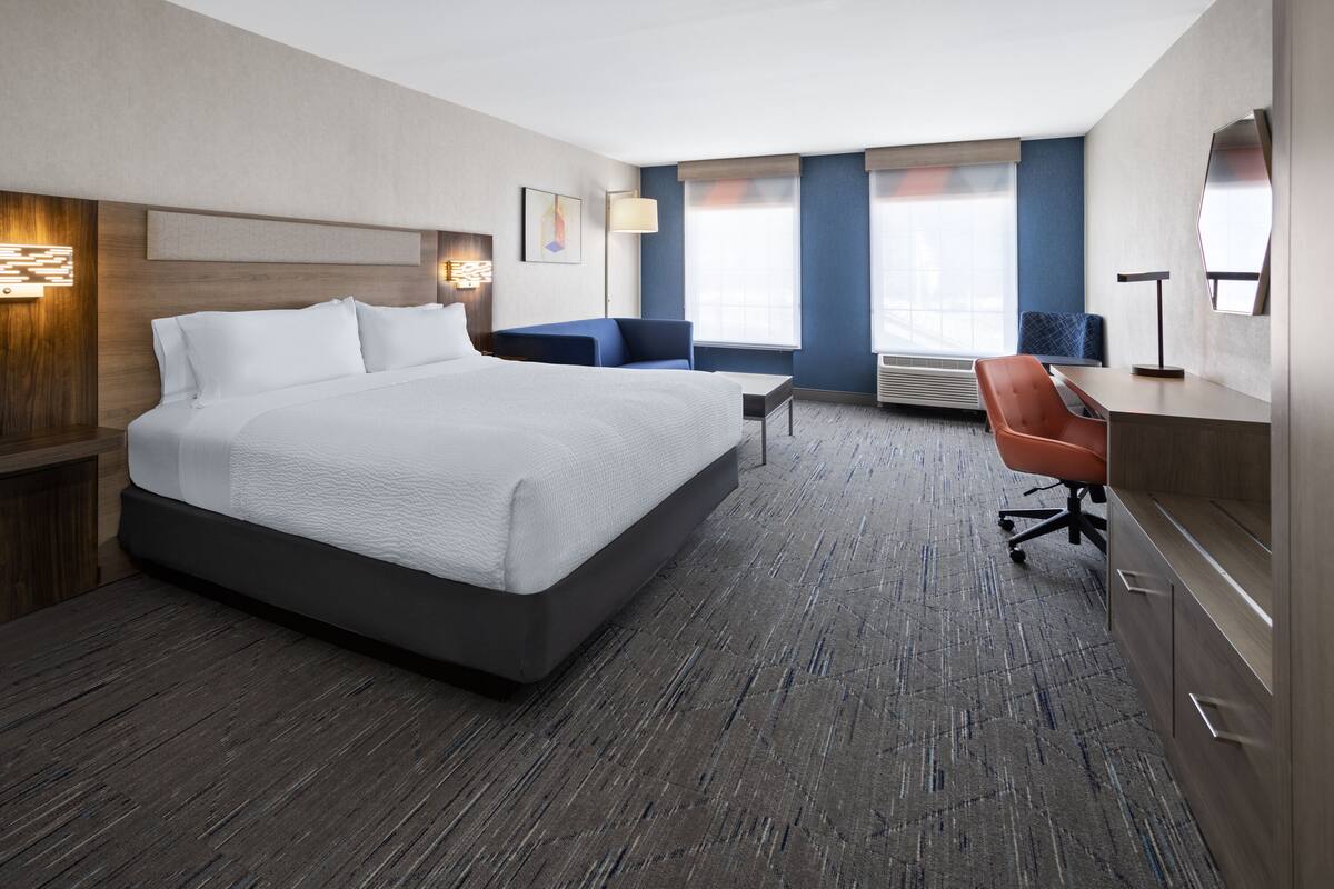 A hotel room with a large bed, a desk, a chair, and a window with blinds.
