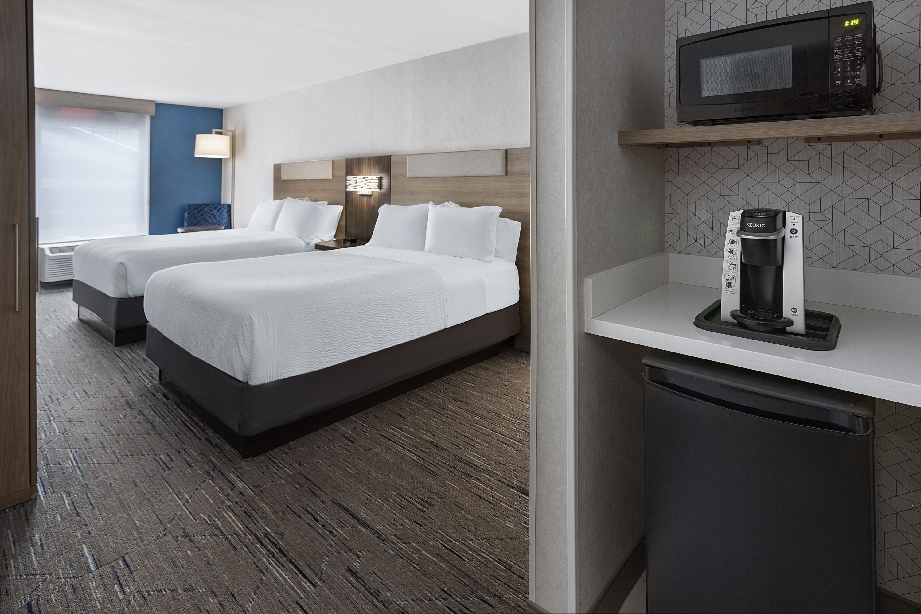 A hotel room with two beds, a microwave, a coffee maker, and a small refrigerator.