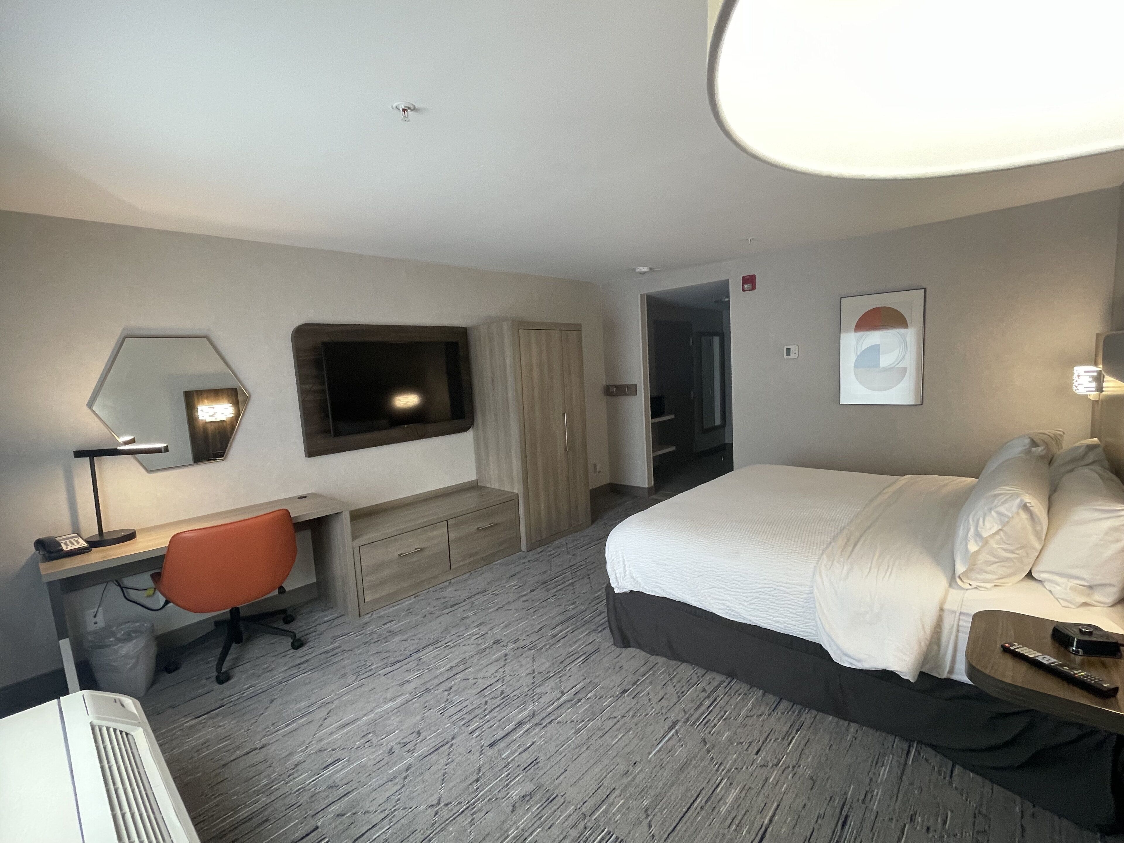 Une chambre d’hôtel comprenant un lit, un bureau avec une chaise, un téléviseur fixé au mur et une porte donnant sur une autre pièce.