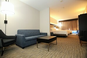 A hotel room with a blue sofa, a black coffee table, a bed with white linens, and a large window with curtains. - Holiday Inn Express & Suites Ashland by IHG (Ashland)