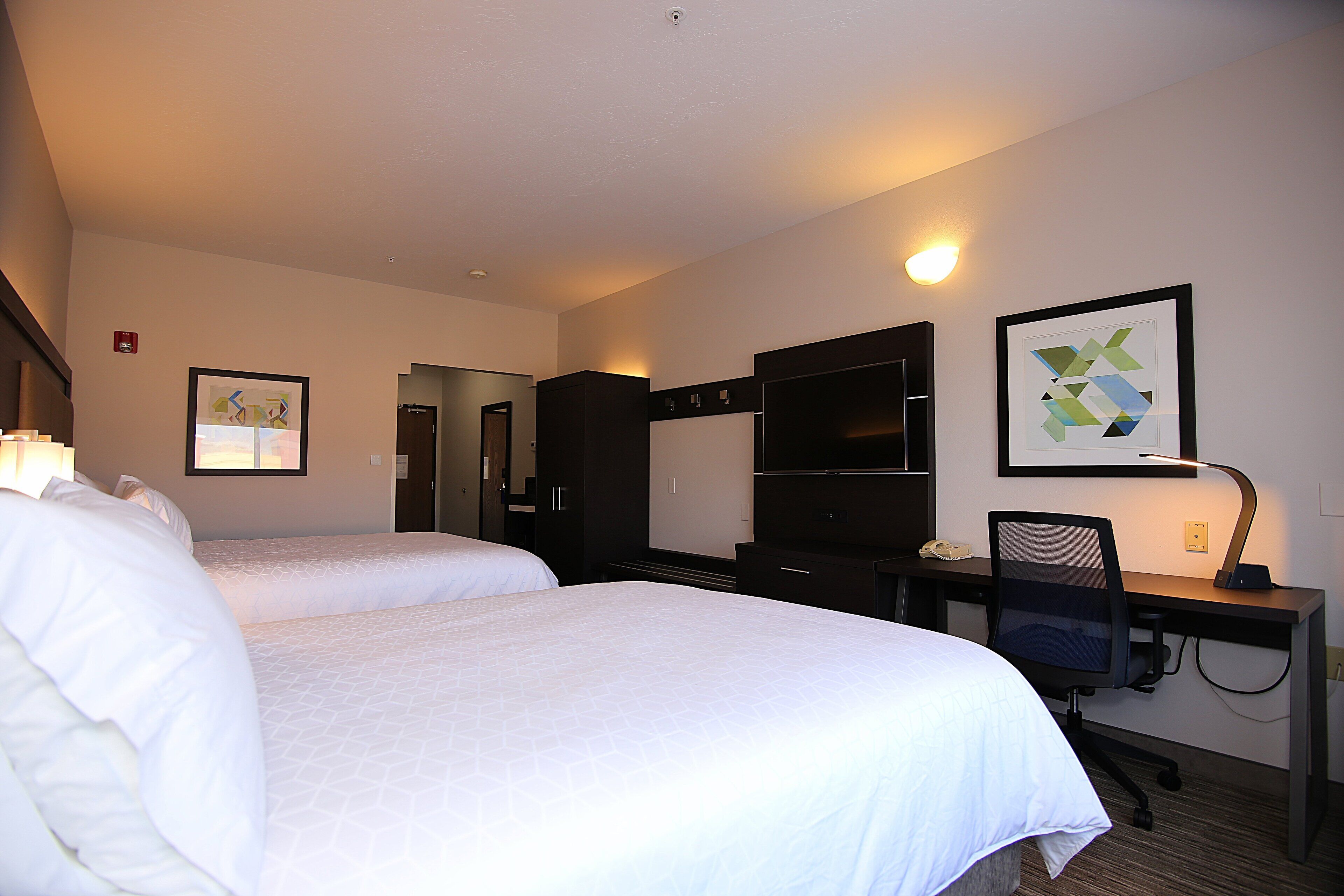Une chambre d’hôtel avec deux lits, un bureau avec une chaise, une télévision et un tableau encadré au mur.