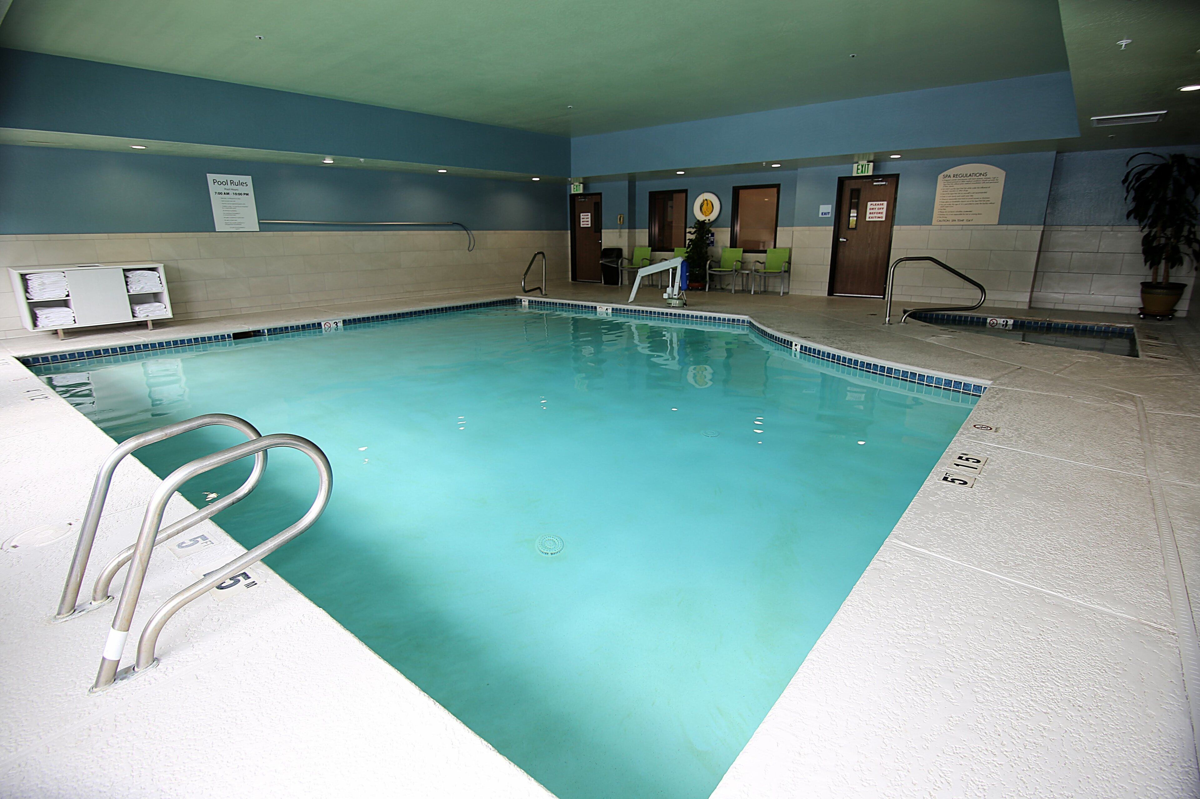 An indoor swimming pool with clear water, a pool ladder, and a sign indicating pool rules.