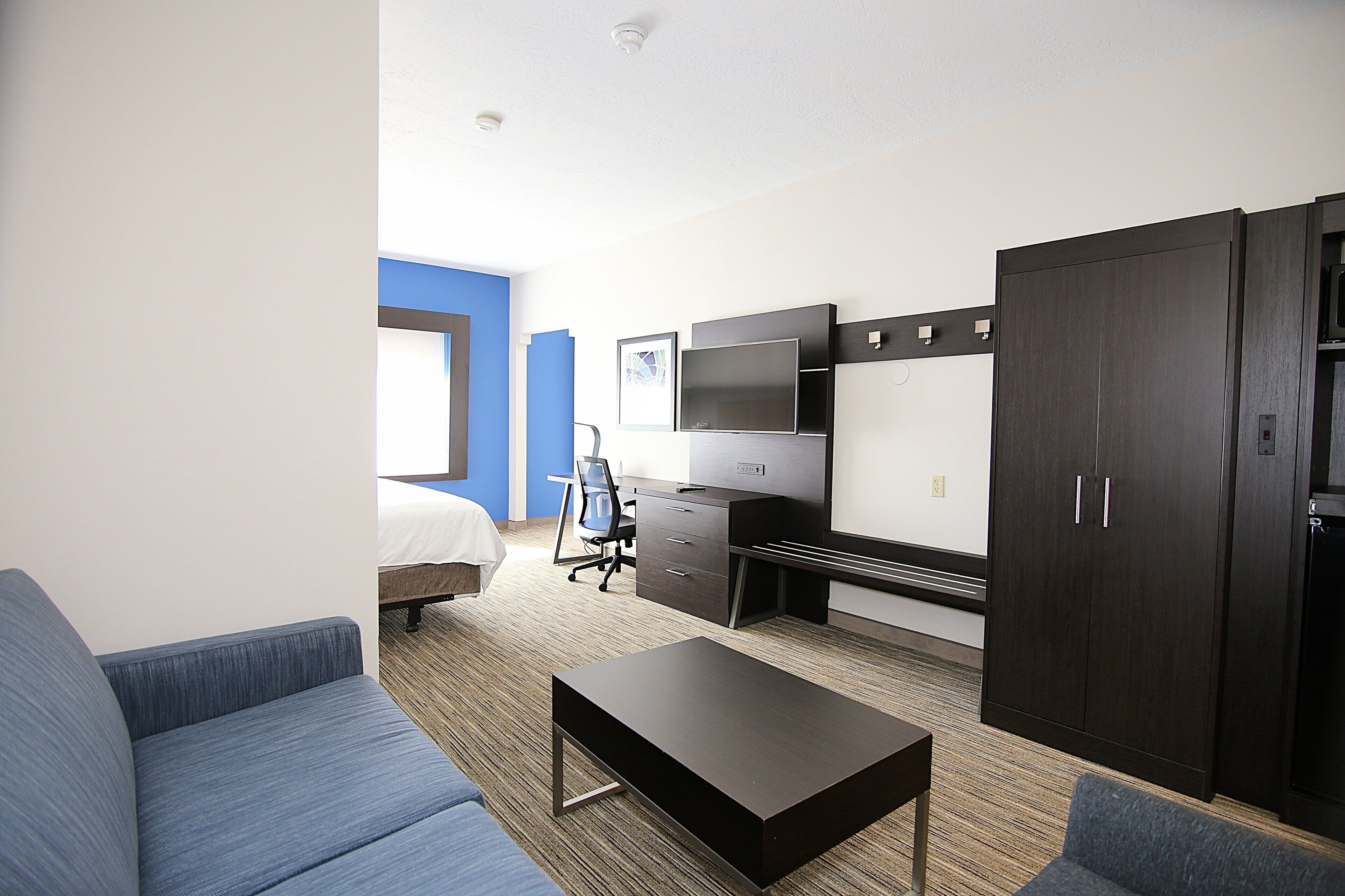 Ett hotellrum med en säng, ett skrivbord, en tv, en garderob och en soffa.