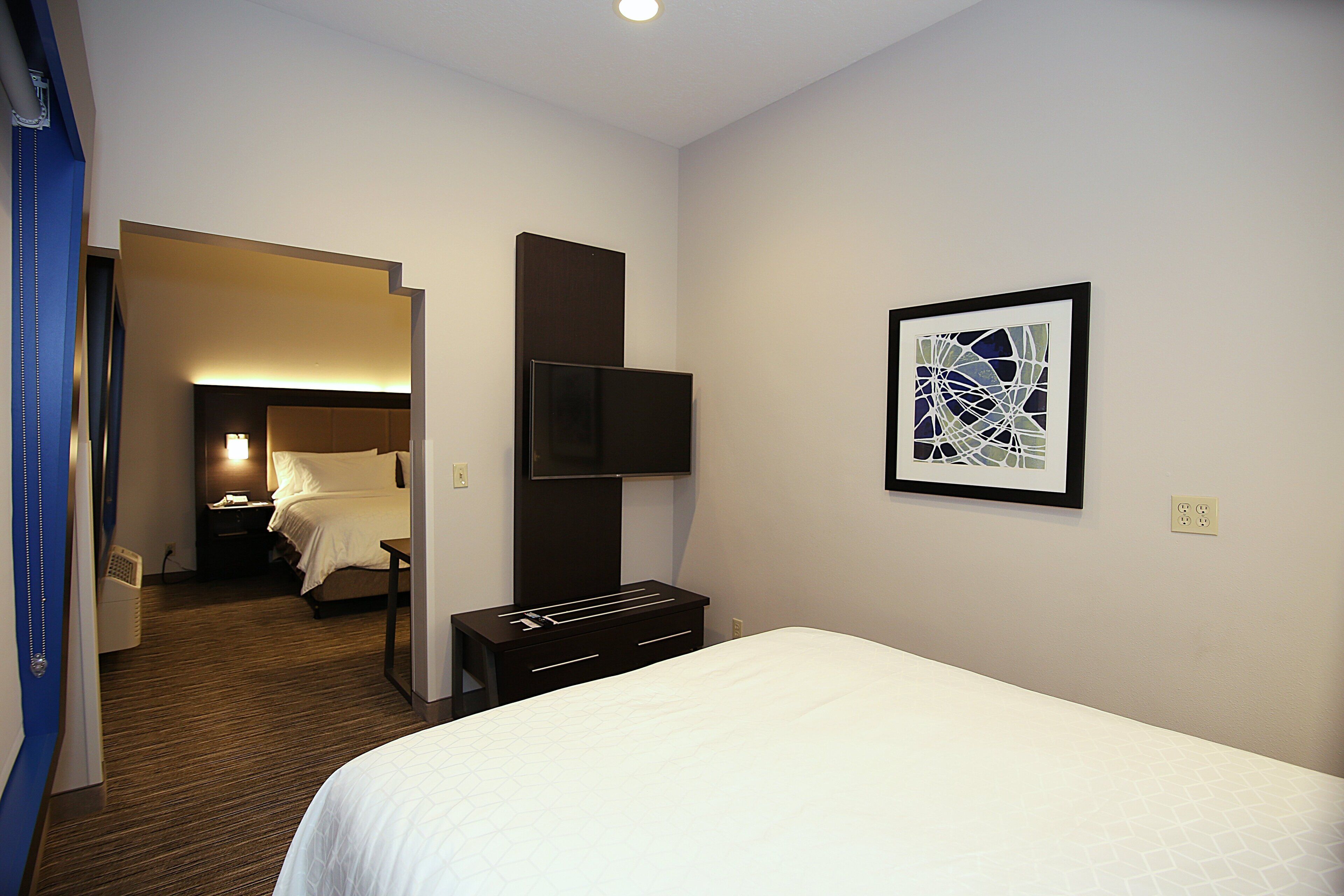 A hotel room with a bed, a flat-screen TV mounted on the wall, a bedside table, and a framed abstract artwork.