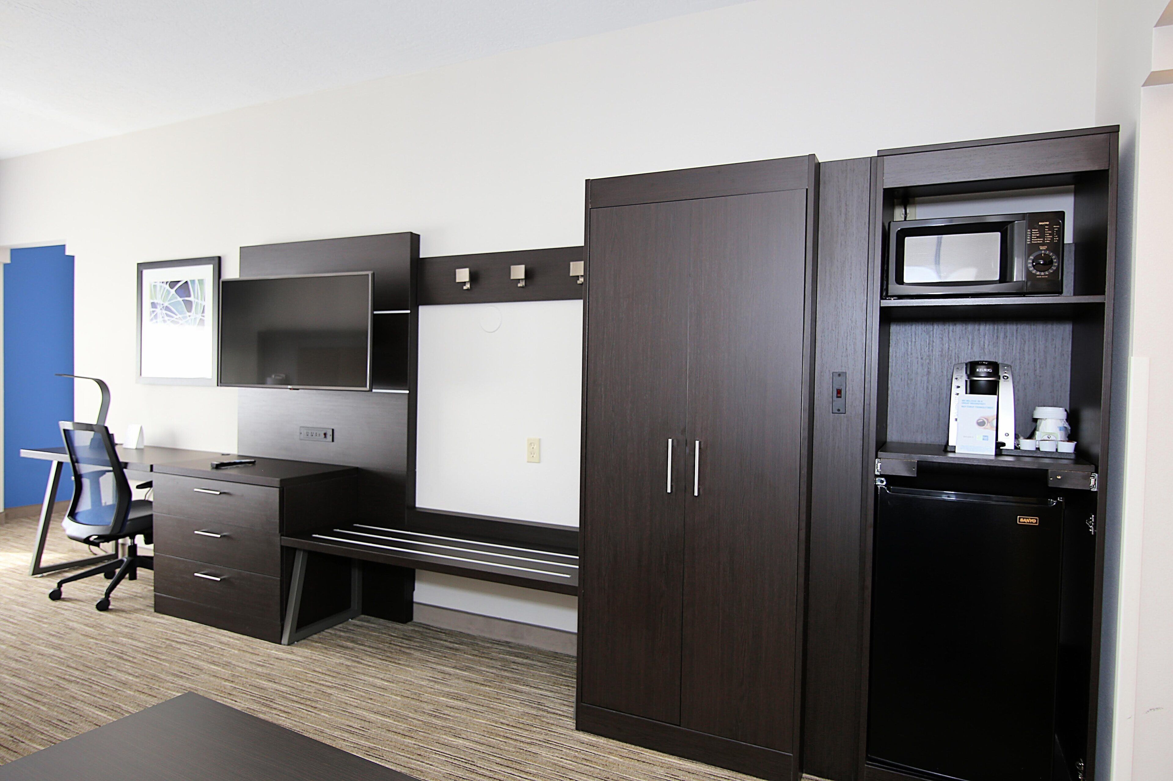 A compact office space with a desk, chair, wardrobe, and a microwave.