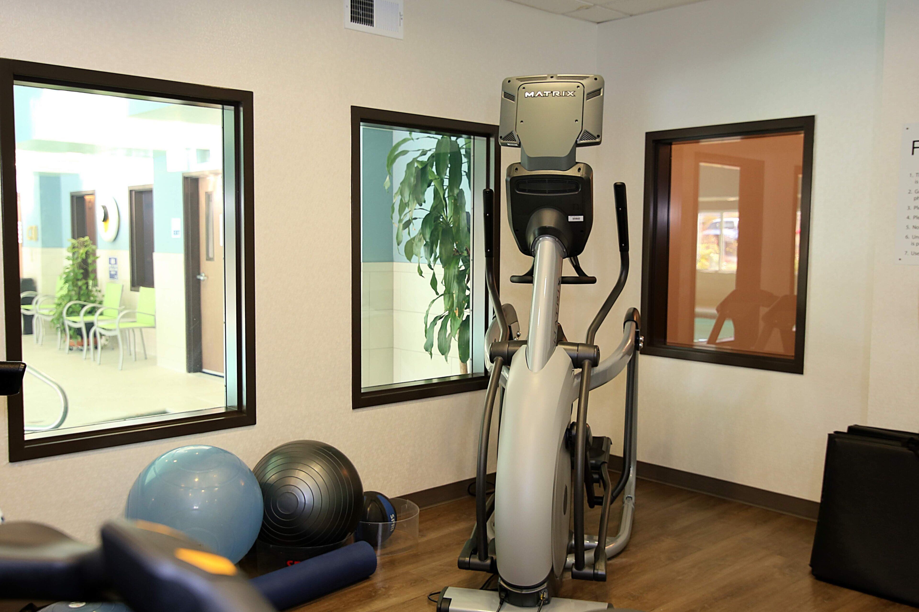 A fitness room with an elliptical machine, exercise balls, and a mirror.