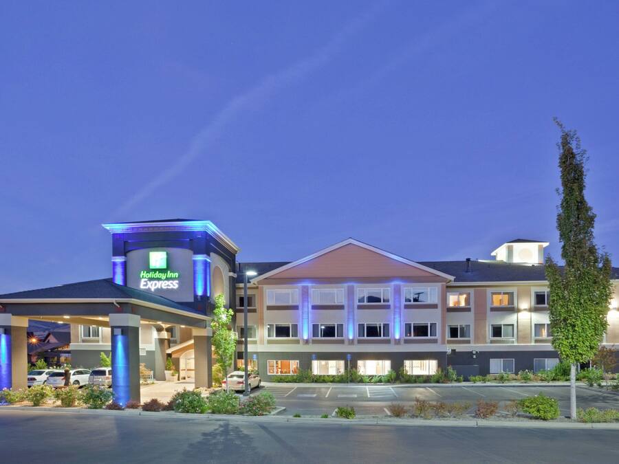A Holiday Inn Express hotel with a two-story structure, a parking lot, and a landscaped area with shrubs and a tall tree.