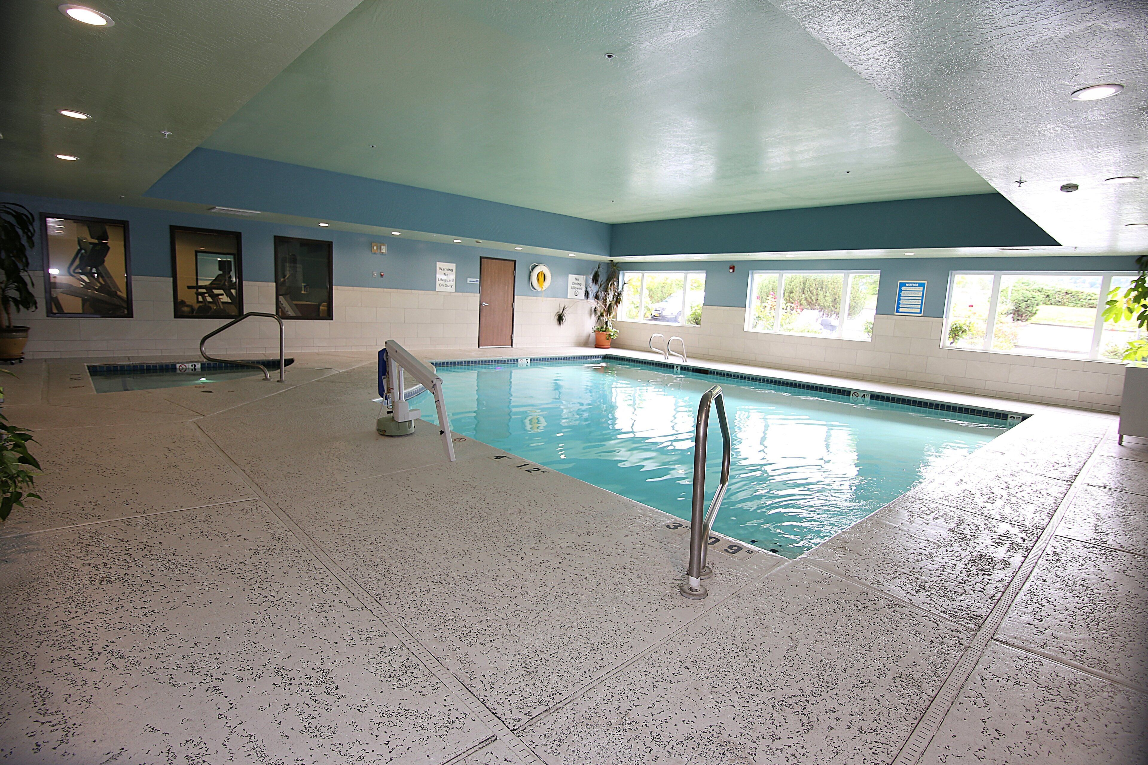 Una piscina interior con agua cristalina, un trampolín y una silla para salvavidas.