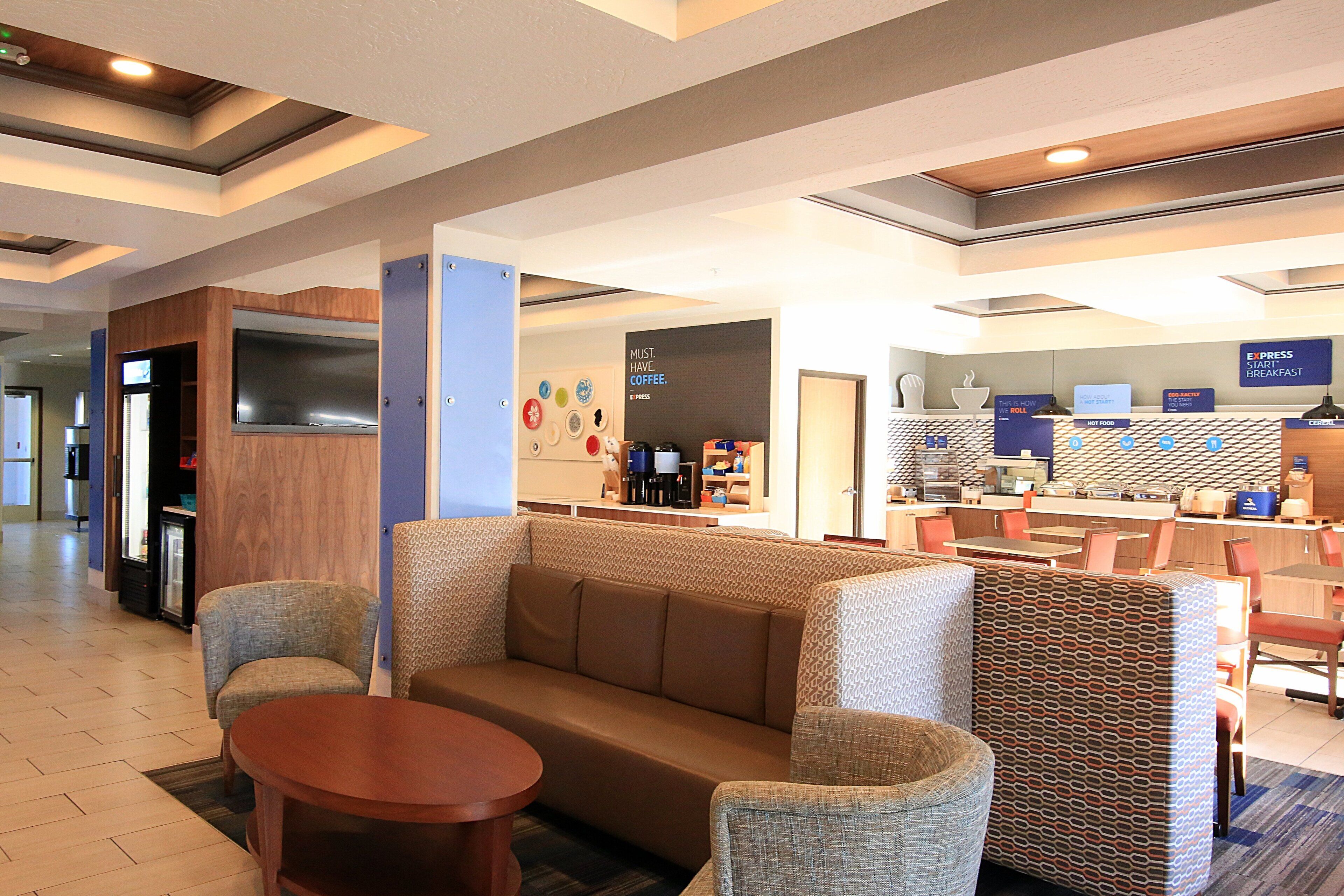 A hotel lobby with seating areas, a coffee station, and a breakfast bar.