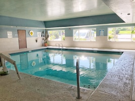 An indoor swimming pool with clear water, a diving board, and a lifeguard sign.