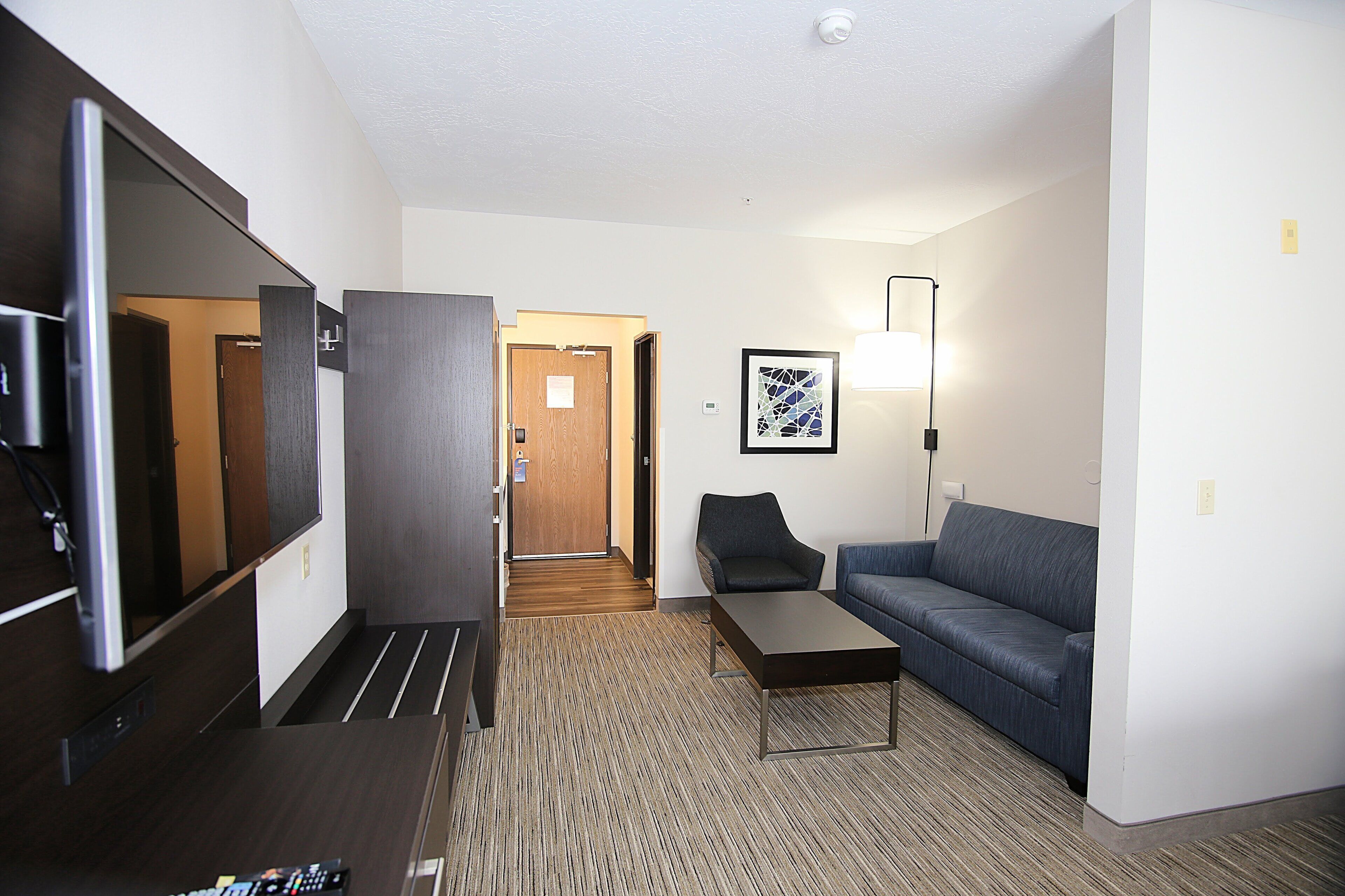 A hotel room with a flat-screen TV, a sofa, a small table, a lamp, and a framed picture on the wall.