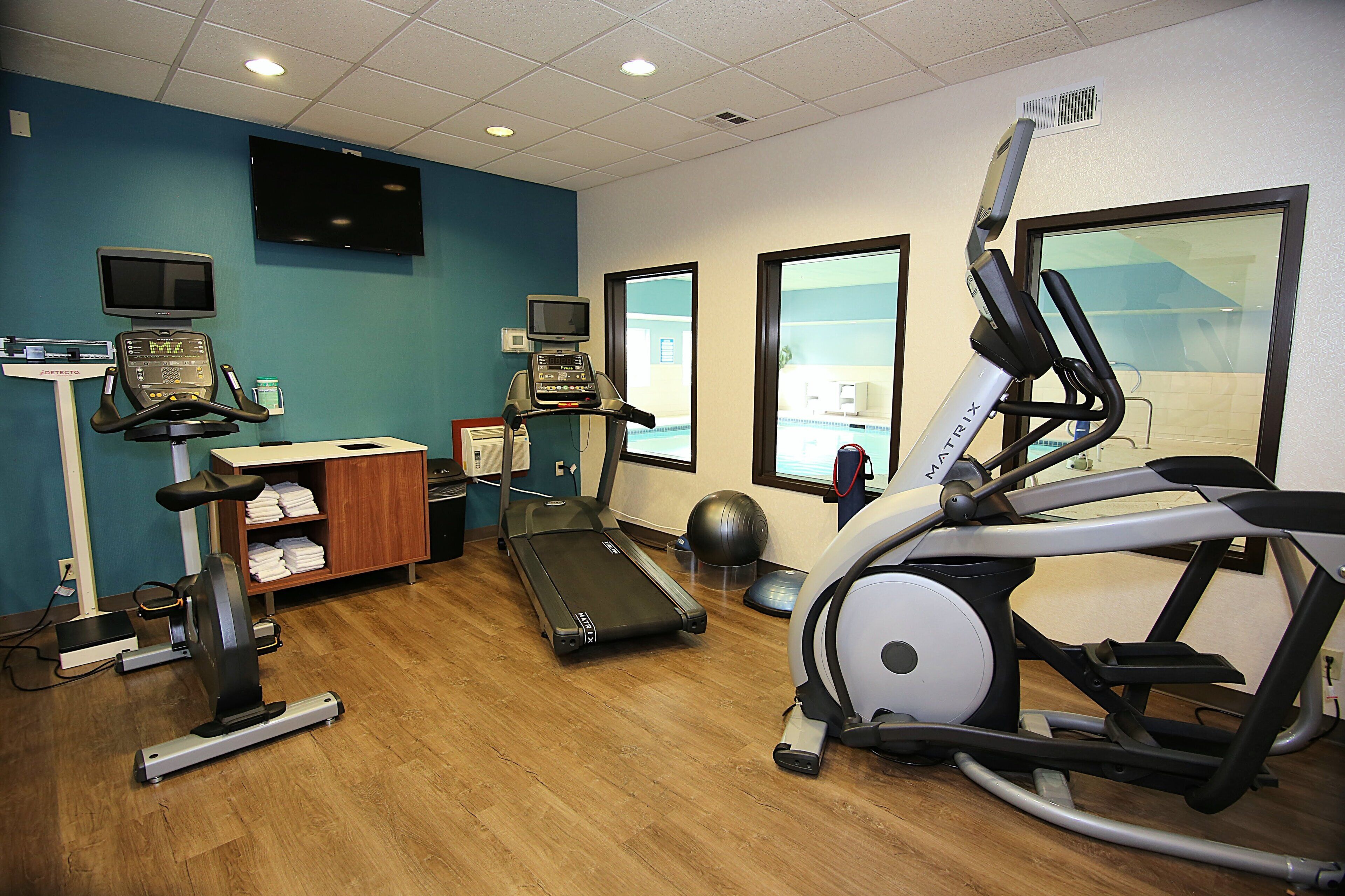 Ein Fitnessstudio mit Laufbändern, einem Crosstrainer, einem stationären Fahrrad und einer Gewichtbank.