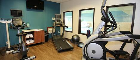 Ein Fitnessstudio mit Laufbändern, einem Crosstrainer, einem stationären Fahrrad und einer Gewichtbank.