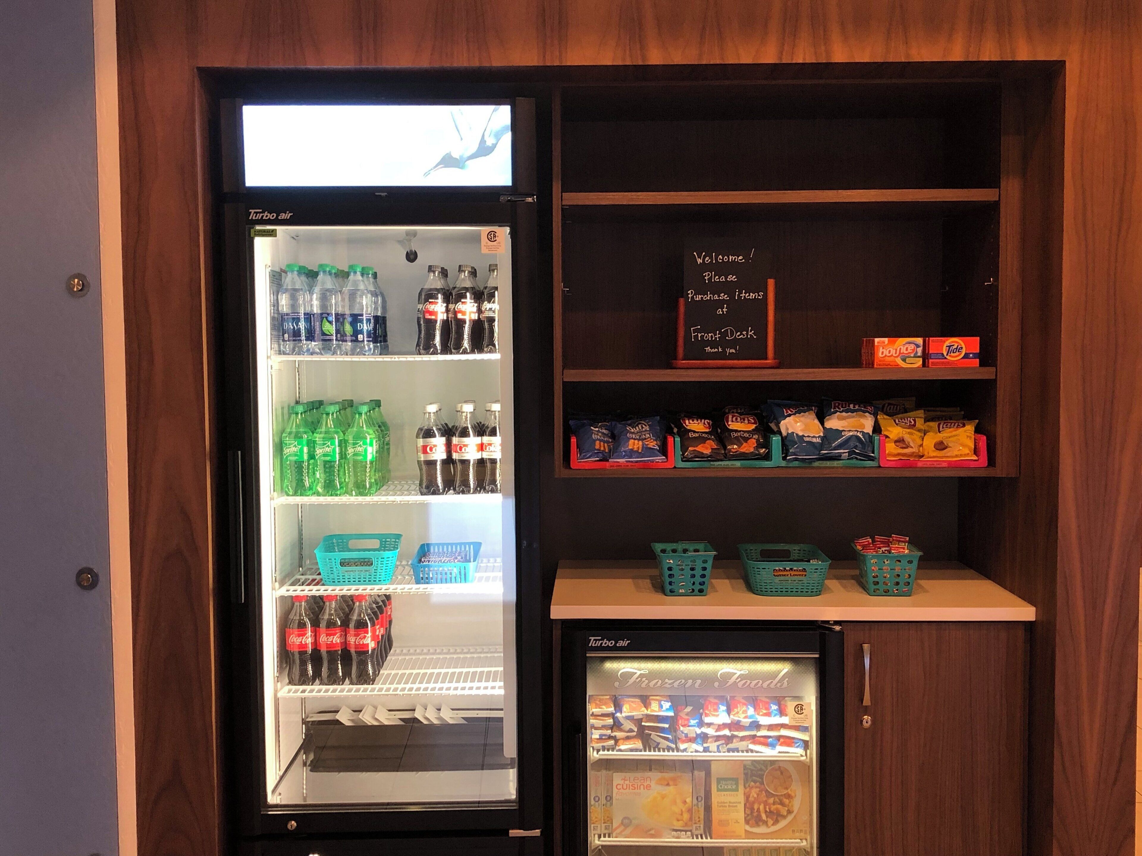 Un distributeur automatique proposant diverses boissons et collations, un comptoir d’accueil avec un panneau de bienvenue et un rayon réfrigéré étiqueté « Aliments surgelés ».