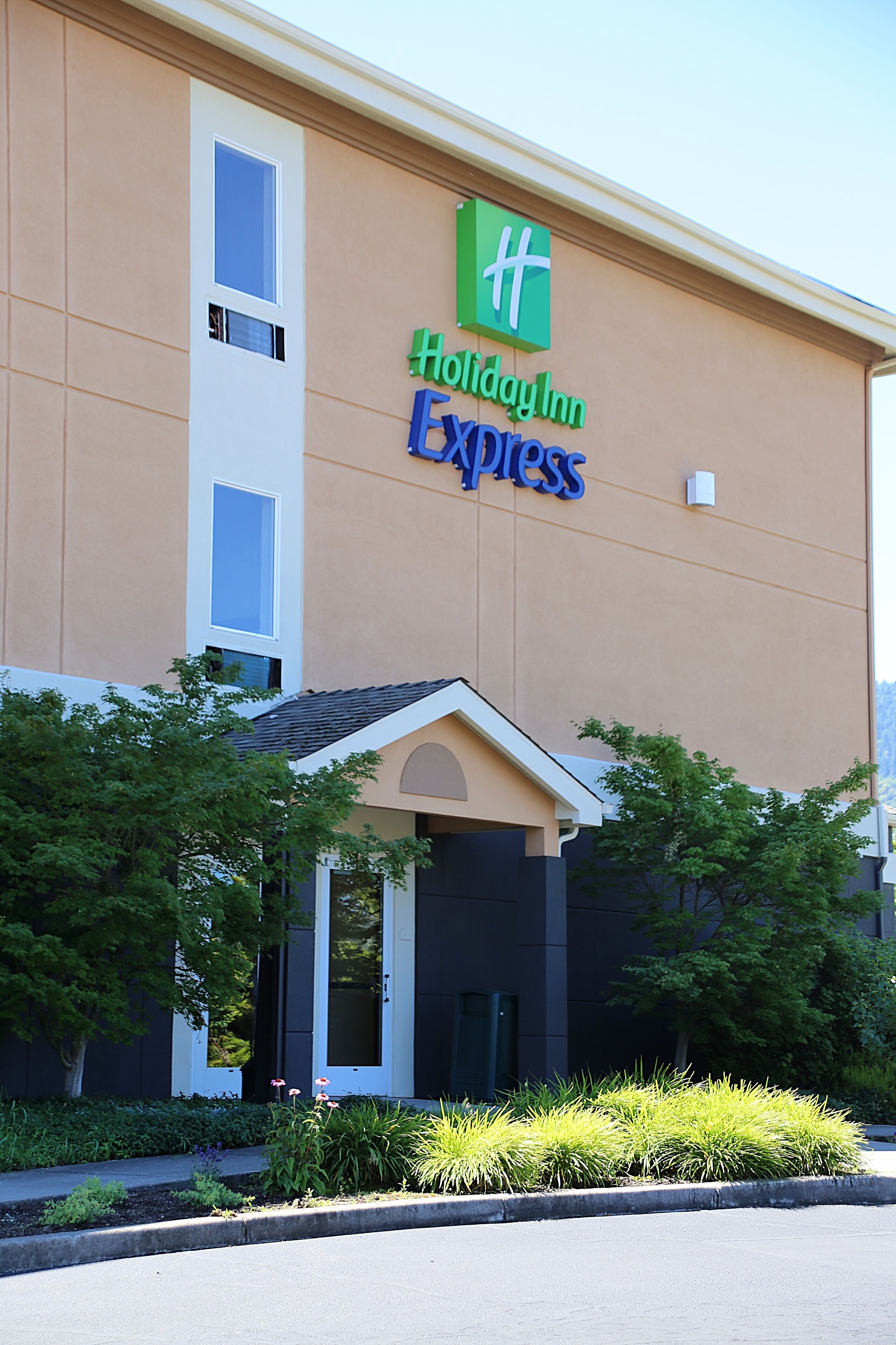 A Holiday Inn Express building with a green and blue sign, a covered entrance, and landscaped greenery.