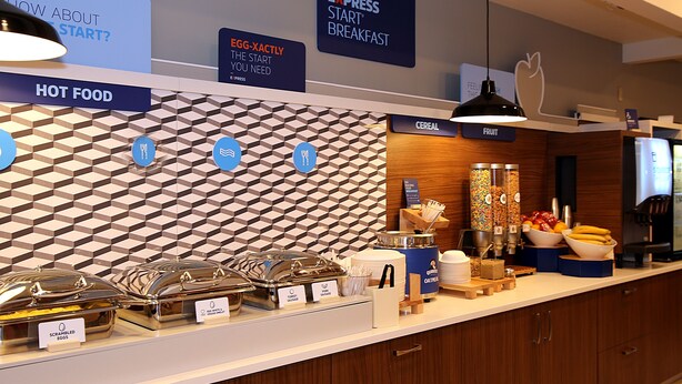 A breakfast buffet area with labeled food stations, including hot food, cereal, and fruit.