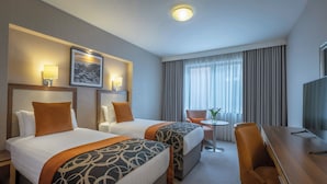 Ein Hotelzimmer mit zwei Betten, einem Schreibtisch, einem Stuhl, einem Fernseher und einem Fenster mit Vorhängen.