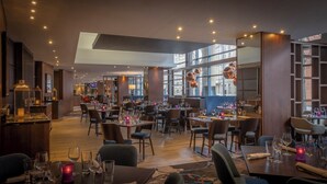 Ein modernes Restaurant mit verschiedenen Essbereichen, großen Fenstern und zeitgenössischen Leuchten.